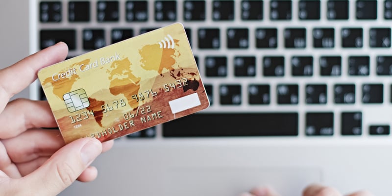 Hombre con una tarjeta de credito en la mano sobre una computadora.