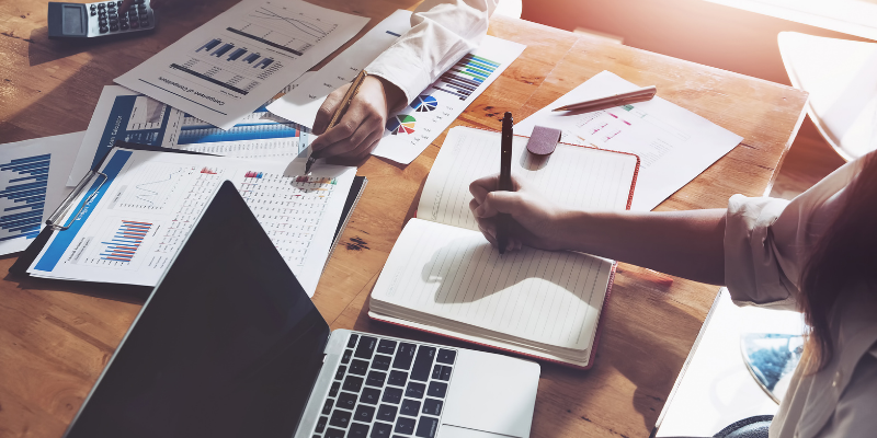Mujer escribiendo en su liberta de notas junto a su computador.